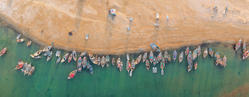 Aerial view of numerous colorful fishing boats moored along the sandy shoreline of the turquoise sea Gwadar Balochistan Pakistan.