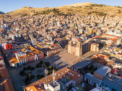 Aerial view of the historic Puno Cathedral and Plaza de Armas surrounded by dense urban rooftops and mountainous landscape in Puno Puno Peru.
