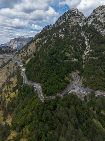 Aerial view of the winding mountain road through the lush forests and rocky slopes of the Albanian Alps in Shkoder Shkoder County Albania. Aerial view of the winding mountain road through the lush forests and rocky slopes of the Albanian Alps in Shkoder Shkoder County Albania.