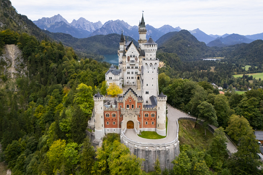 Aerial view of the majestic Neuschwanstein Castle rising amidst lush forests with a backdrop of towering mountains Neuschwanstein Castle Bayern Germany. Aerial view of the majestic Neuschwanstein Castle rising amidst lush forests with a backdrop of towering mountains Neuschwanstein Castle Bayern Germany.