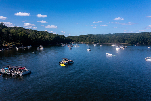 Aerial view of Lake Wallenpaupack with pontoon boats and recreational vessels on the water surrounded by dense forests under a clear blue sky in Tannersville Pennsylvania United States.