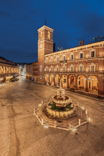 View of the historic Piazza del Comune in Fabriano featuring the illuminated Fontana Sturinalto and the clock tower of the Palazzo del Podesta at dusk Fabriano Marche Italy. View of the historic Piazza del Comune in Fabriano featuring the illuminated Fontana Sturinalto and the clock tower of the Palazzo del Podesta at dusk Fabriano Marche Italy.