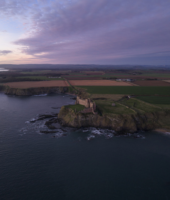 Aerial view of Tantallon Castle on a rocky cliff overlooking the North Sea under a purple sunset sky North Berwick Scotland United Kingdom.