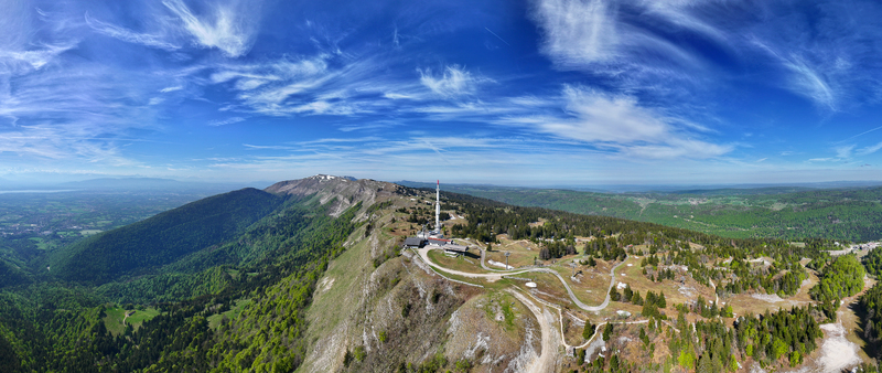 Aerial view of Col de la Faucille mountain pass with its telecommunications tower winding roads and lush green slopes under a blue sky Gex Auvergne Rhone Alpes France. Aerial view of Col de la Faucille mountain pass with its telecommunications tower winding roads and lush green slopes under a blue sky Gex Auvergne Rhone Alpes France.