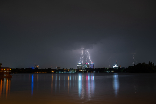 View of lightning strikes illuminating the night skyline across the lake with reflections on the water surface in Bucharest Bucharest Romania. View of lightning strikes illuminating the night skyline across the lake with reflections on the water surface in Bucharest Bucharest Romania.