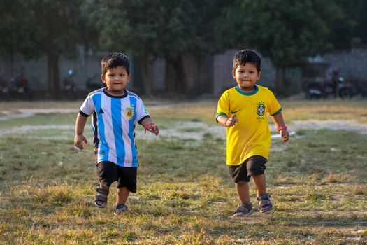Bogura Bangladesh 18 November 2022 View of two young boys wearing football jerseys running across a grassy field in the late afternoon light.