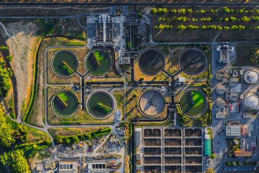 Aerial view of a water treatment plant featuring circular sedimentation tanks filtration basins and industrial infrastructure surrounded by green fields in Rome Lazio Italy.