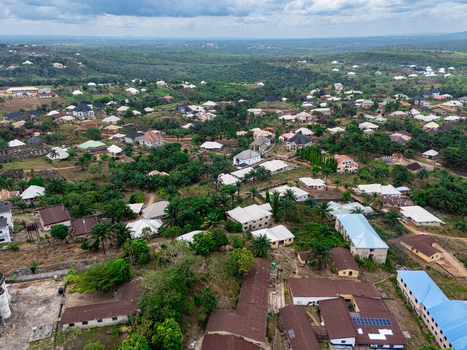 Aerial view of a sprawling settlement with diverse rooflines nestled amidst a verdant canopy featuring a prominent blue roofed building under a cloudy sky Asaga Abia Nigeria. Aerial view of a sprawling settlement with diverse rooflines nestled amidst a verdant canopy featuring a prominent blue roofed building under a cloudy sky Asaga Abia Nigeria.