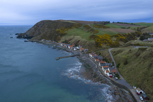 Aerial view of the historic cottages of Crovie nestled at the base of steep cliffs along the rugged North Sea coastline Crovie Scotland United Kingdom.
