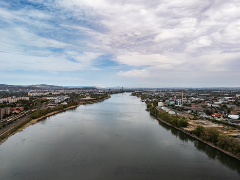 Aerial view of the Danube River flowing between the industrial Csepel and Budafok districts with factories riverside roads and the urban skyline of Budapest Hungary. Aerial view of the Danube River flowing between the industrial Csepel and Budafok districts with factories riverside roads and the urban skyline of Budapest Hungary.