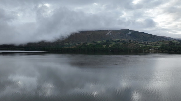 Aerial view of Corani Lake with calm water reflecting the cloudy sky and mist covered mountains in the background in Chapare Cochabamba Department Bolivia. Aerial view of Corani Lake with calm water reflecting the cloudy sky and mist covered mountains in the background in Chapare Cochabamba Department Bolivia.