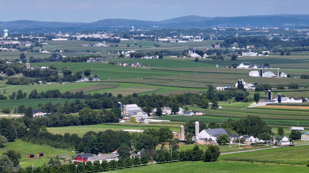 Aerial view of the rural landscape in Ronks featuring lush green farmland traditional barns silos and rolling hills under a clear sky in Ronks Pennsylvania United States.