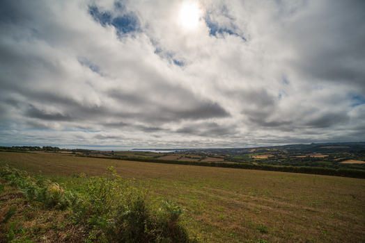 View of rolling fields and lush countryside overlooking the Fowey River estuary under a dramatic cloudy sky in Fowey Cornwall United Kingdom. View of rolling fields and lush countryside overlooking the Fowey River estuary under a dramatic cloudy sky in Fowey Cornwall United Kingdom.