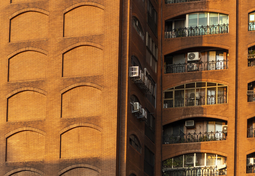 View of the red brick facade of a residential building with arched balconies and air conditioning units under warm sunlight Taipei City Taiwan. View of the red brick facade of a residential building with arched balconies and air conditioning units under warm sunlight Taipei City Taiwan.