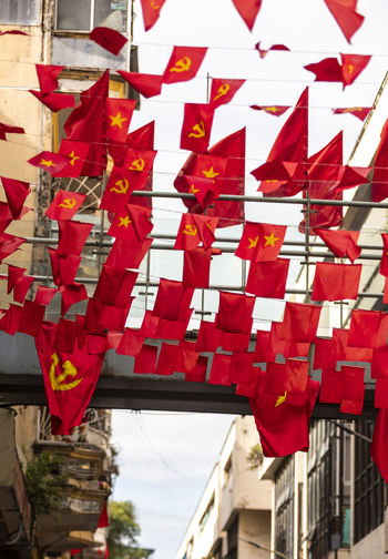 View of numerous red flags with yellow stars and hammers and sickles hanging over a narrow street in the historic city center of Hanoi Ha Noi Vietnam.
