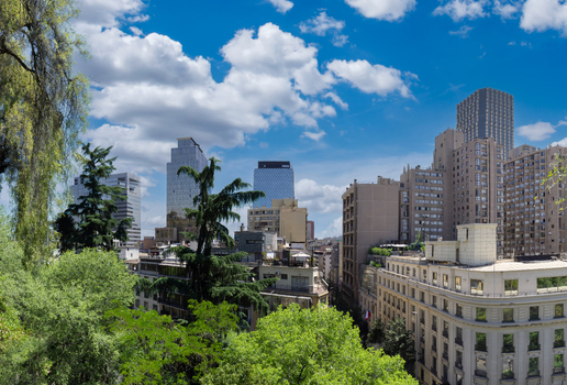 Aerial view of the modern cityscape of Santiago with lush green trees in the foreground high rise buildings and a bright blue sky in Santiago Santiago Metropolitan Chile.