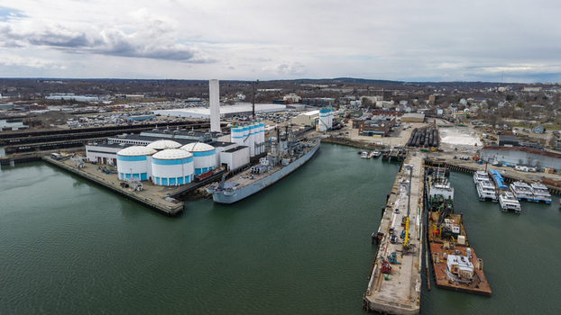 Aerial view of the USS Salem resting in the Fore River surrounded by bright white storage tanks and a working dry dock Quincy Massachusetts United States.