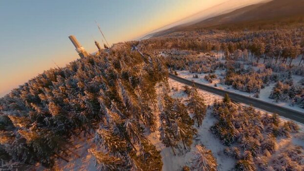 FPV aerial view of snowy forest and tower in Germany.