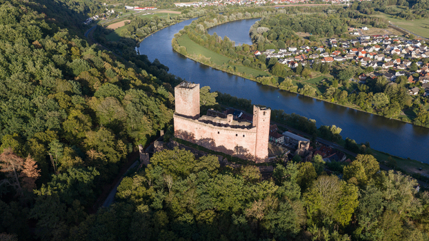 Aerial view of Henneburg castle ruins surrounded by dense forest overlooking the Main river and the town of Stadtprozelten Bayern Germany.