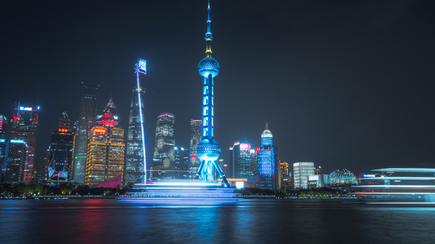 View of the Oriental Pearl Tower and the illuminated Pudong skyline at night with light trails from boats on the Huangpu River in Shanghai Shanghai China.