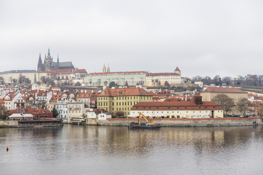 View of Prague Castle and historic red roofed buildings along the Vltava River under an overcast sky in Prague Prague Czechia. View of Prague Castle and historic red roofed buildings along the Vltava River under an overcast sky in Prague Prague Czechia.