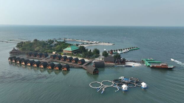 Aerial view of Pulau Lima Resort featuring overwater bungalows a wooden pier and circular fish farming cages in the calm sea near Kasemen Banten Indonesia. Aerial view of Pulau Lima Resort featuring overwater bungalows a wooden pier and circular fish farming cages in the calm sea near Kasemen Banten Indonesia.