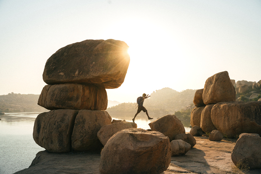 View of a person jumping between large granite boulders near the river during sunset in Hampi Karnataka India. View of a person jumping between large granite boulders near the river during sunset in Hampi Karnataka India.
