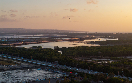 Aerial view of Bali Mandara Toll Road stretching across the mangrove forest and coastal waters at sunset in Kecamatan Kuta Selatan Bali Indonesia.