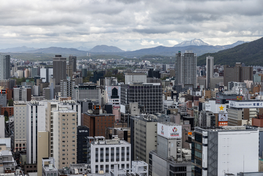 Aerial view of the dense urban skyline of Sapporo with modern high rise buildings and office towers set against a backdrop of mountains under a cloudy sky in Sapporo Hokkaido Japan. Aerial view of the dense urban skyline of Sapporo with modern high rise buildings and office towers set against a backdrop of mountains under a cloudy sky in Sapporo Hokkaido Japan.