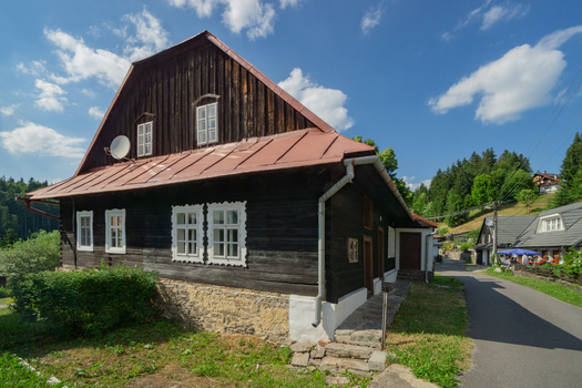 View of a rustic wooden house with stone foundation and red roof stands under a blue sky with fluffy clouds in Polianka Donovaly Banskobystricky kraj Slovakia. View of a rustic wooden house with stone foundation and red roof stands under a blue sky with fluffy clouds in Polianka Donovaly Banskobystricky kraj Slovakia.