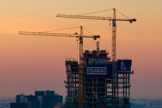Warsaw Poland 01 March 2026 Aerial view of the Upper One skyscraper under construction with tower cranes and Strabag signage against a sunset sky.
