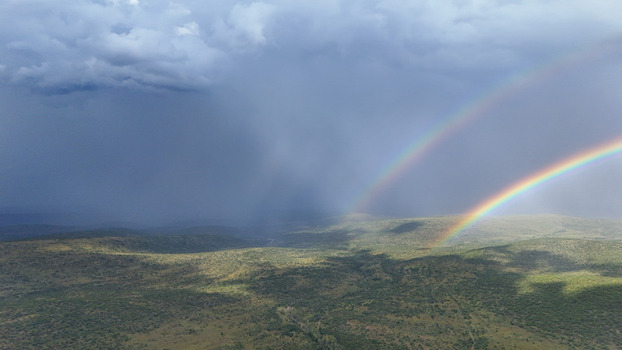 Aerial view of a double rainbow stretching across a vast green landscape under dark storm clouds in Waterberg District Municipality Limpopo South Africa. Aerial view of a double rainbow stretching across a vast green landscape under dark storm clouds in Waterberg District Municipality Limpopo South Africa.