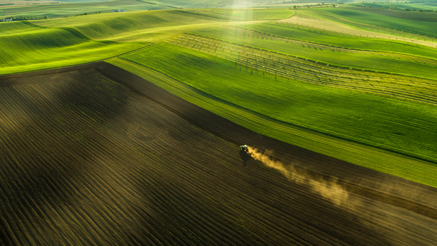Aerial view of a tractor plowing a field in the rolling landscape of Moravia creating dust trails under the golden hour light in Brno City District South Moravian Region Czechia.