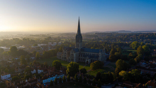 Aerial view of Salisbury Cathedral surrounded by historic rooftops and lush greenery during the golden hour in Salisbury England United Kingdom. Aerial view of Salisbury Cathedral surrounded by historic rooftops and lush greenery during the golden hour in Salisbury England United Kingdom.