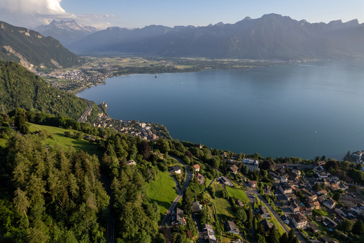 Aerial view of the village of Glion overlooking Lake Geneva with lush green hills residential houses winding roads and the Swiss Alps in the background in Montreux Vaud Switzerland. Aerial view of the village of Glion overlooking Lake Geneva with lush green hills residential houses winding roads and the Swiss Alps in the background in Montreux Vaud Switzerland.