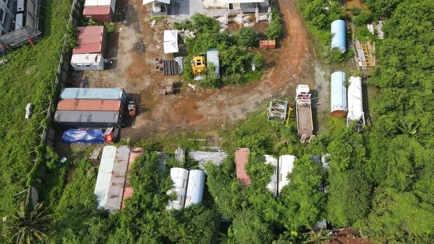 Aerial view of Bambu Apus site featuring shipping containers large cylindrical tanks and a truck parked amidst lush vegetation in Kecamatan Cipayung Daerah Khusus Ibukota Indonesia. Aerial view of Bambu Apus site featuring shipping containers large cylindrical tanks and a truck parked amidst lush vegetation in Kecamatan Cipayung Daerah Khusus Ibukota Indonesia.