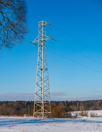 View of a metal electricity pylon standing in a snow covered field under a clear blue sky with a forest in the background in Vilnius Vilniaus apskritis Lithuania. View of a metal electricity pylon standing in a snow covered field under a clear blue sky with a forest in the background in Vilnius Vilniaus apskritis Lithuania.