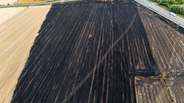 Aerial view of a partially burned agricultural field with charred soil next to a golden harvested crop area adjacent to a road with a truck in Sremska Mitrovica Vojvodina Serbia.