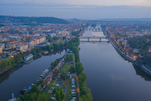 Aerial view of the Vltava River in Prague featuring multiple bridges boats moored along the bank and the cityscape under a soft twilight sky in Prague Prague Czechia.