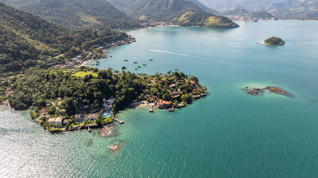 Aerial view of Ilha de Cataguas featuring lush tropical vegetation coastal houses with private docks and clear turquoise waters in Angra dos Reis Rio de Janeiro Brazil.