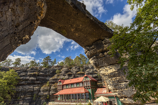 View of Pravcicka Brana the largest natural sandstone arch in Europe with the historic Sokoli hnizdo building nestled beneath the rock formation in Hrensko Usti nad Labem Region Czechia.