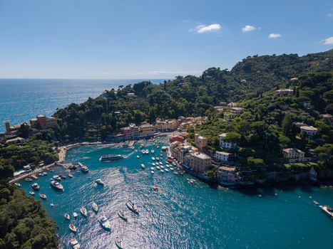 Aerial view of Portofino harbor with colorful buildings and boats moored in the turquoise water surrounded by lush green hills and clear blue sky Portofino Liguria Italy.
