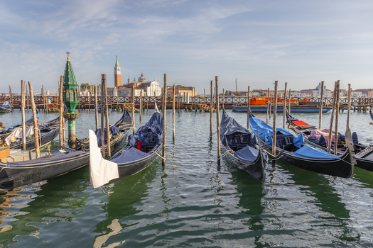 View of gondolas moored at wooden poles in the Venetian lagoon with the historic skyline of Venice in the background under a clear blue sky Venice Veneto Italy. View of gondolas moored at wooden poles in the Venetian lagoon with the historic skyline of Venice in the background under a clear blue sky Venice Veneto Italy.