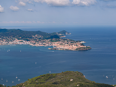 Aerial view of the coastal town of Portoferraio featuring the historic Castello del Volterraio on the distant hill surrounded by the blue Tyrrhenian Sea in Portoferraio Toscana Italy.