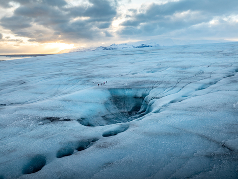 Aerial view of Breidamerkurjokull glacier with people walking across the blue ice surface featuring deep crevasses under a dramatic cloudy sky in Sveitarfelagid Hornafjordur Iceland. Aerial view of Breidamerkurjokull glacier with people walking across the blue ice surface featuring deep crevasses under a dramatic cloudy sky in Sveitarfelagid Hornafjordur Iceland.