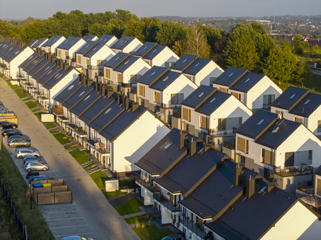 Aerial view of modern terraced houses with dark roofs and white facades surrounded by green trees and parked cars in Wieliczka Lesser Poland Voivode Poland.