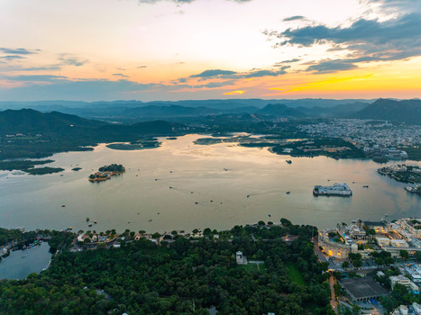 Aerial view of Lake Pichola at sunset with the Lake Palace and Jag Mandir islands surrounded by lush greenery and hills in Udaipur Rajasthan India.