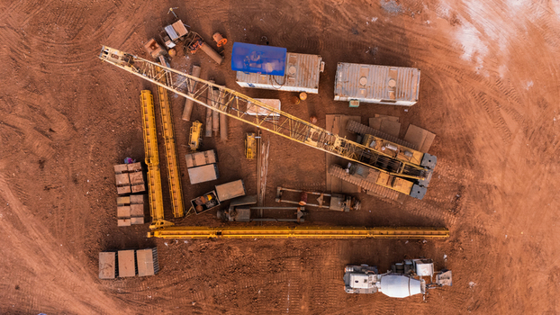 Aerial view of construction equipment including a yellow crane concrete mixer truck and shipping containers at Kawasan Industri Terpadu Batang Kecamatan Gringsing Jawa Tengah Indonesia.