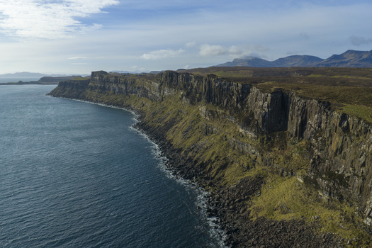 Aerial view of the dramatic basalt cliffs of Kilt Rock and Mealt Falls overlooking the blue ocean and distant mountains Isle of Skye Scotland United Kingdom. Aerial view of the dramatic basalt cliffs of Kilt Rock and Mealt Falls overlooking the blue ocean and distant mountains Isle of Skye Scotland United Kingdom.