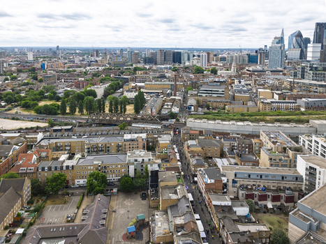 Aerial view of Shoreditch featuring dense urban architecture historic brick buildings modern skyscrapers in the distance and railway lines under a cloudy sky in London England United Kingdom. Aerial view of Shoreditch featuring dense urban architecture historic brick buildings modern skyscrapers in the distance and railway lines under a cloudy sky in London England United Kingdom.